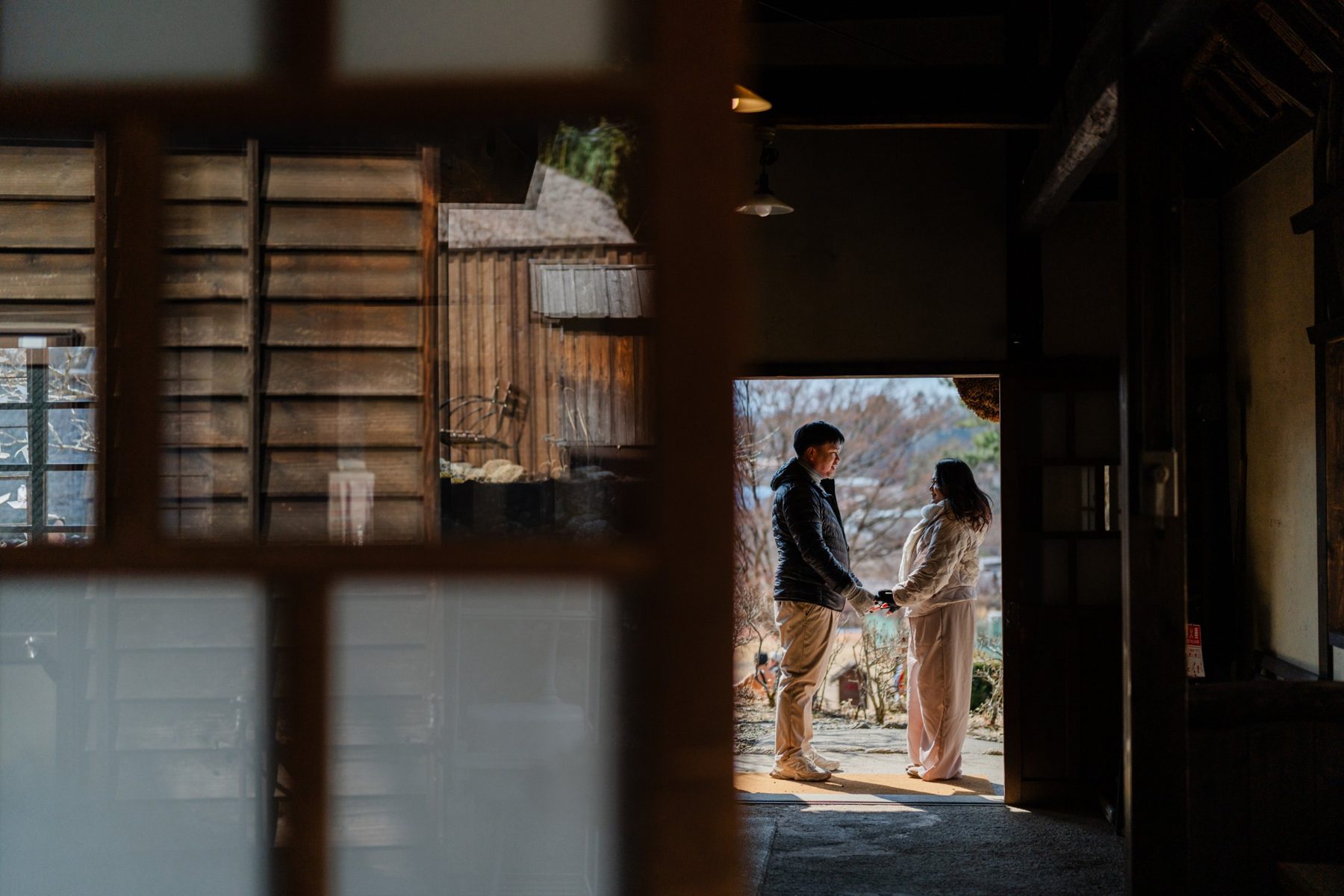 Bazon and Keio holding hands in the light of an old wooden doorway