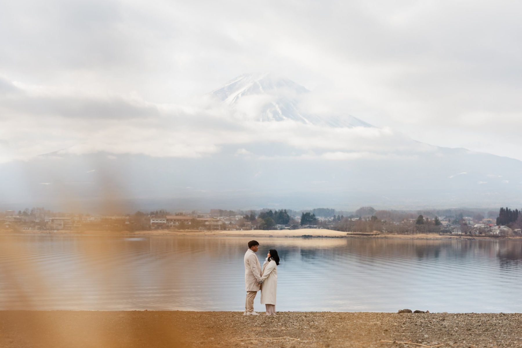 Bazon and Keio holding hands on the shore of a lake, Mt. Fuji rising through clouds behind them